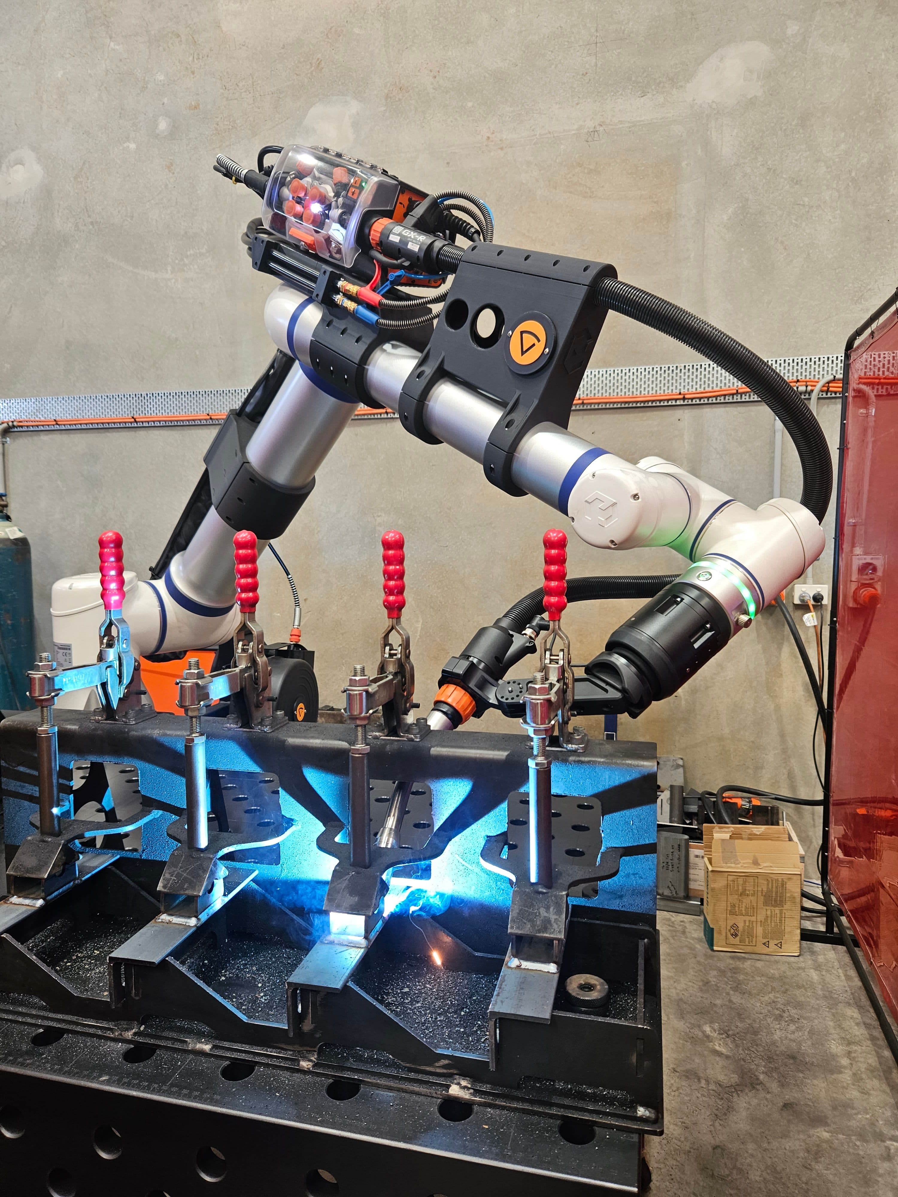 Multi-station fixture with red toggle clamps under cobot welder